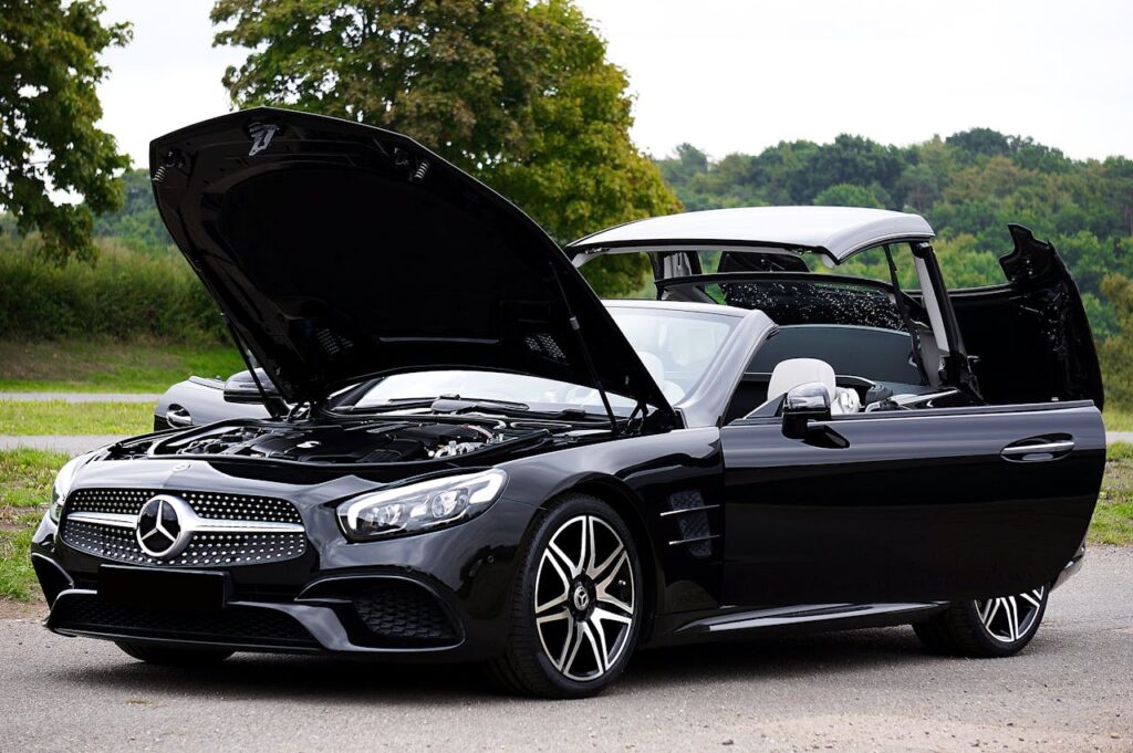 Sleek black convertible car with hood open on a scenic outdoor road.