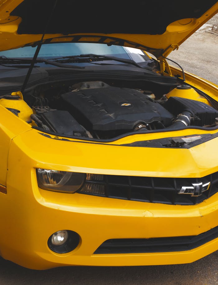 Close-up view of a yellow Chevrolet Camaro with its hood open, showcasing the engine.